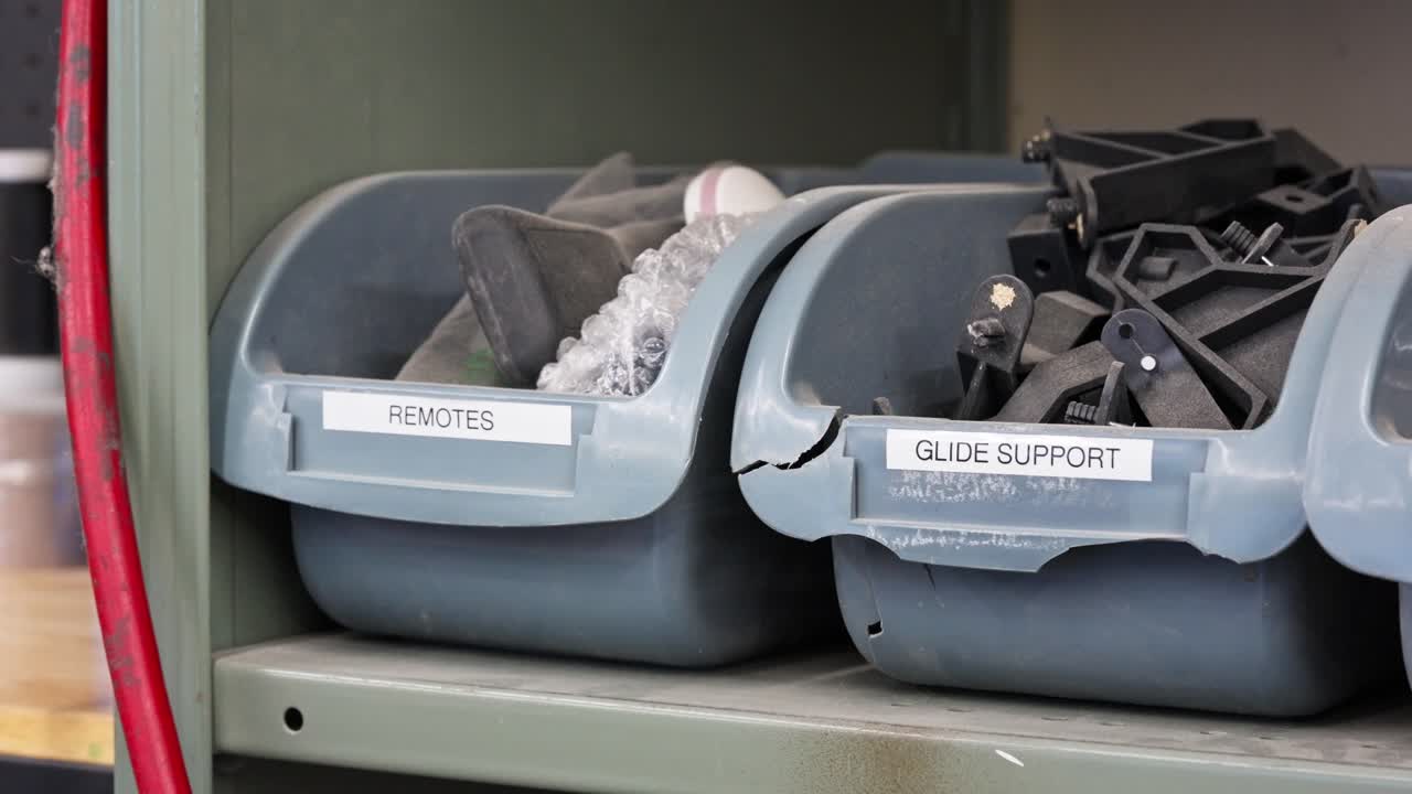 Close pan shows dusty labeled guide support and remotes bins in repair shop