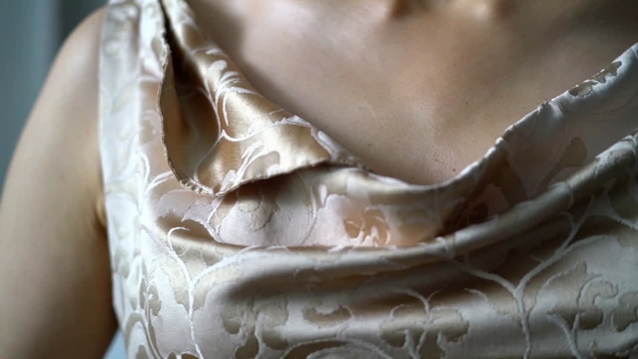 Pulling back camera revealing adult female torso in room to highlight patterned satin cowl neckline