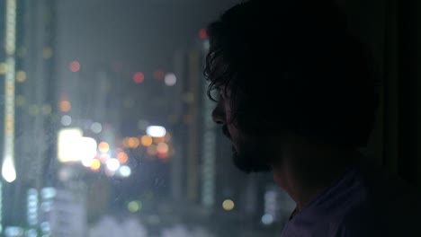 man looking out of city window at night