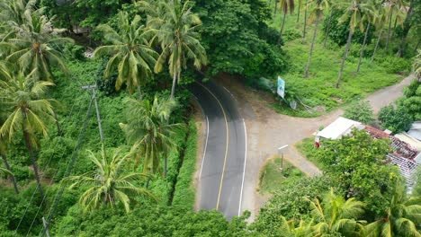 white car and motorbike drive around a bend in the tropical jungle of lombok island, aerial