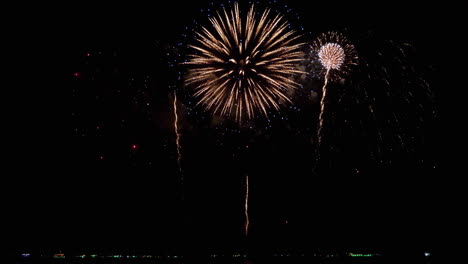 gran diámetro de explosiones blancas seguidas por el mismo patrón pero comienza con naranja luego la base son chispas rojas, exhibición de fuegos artificiales