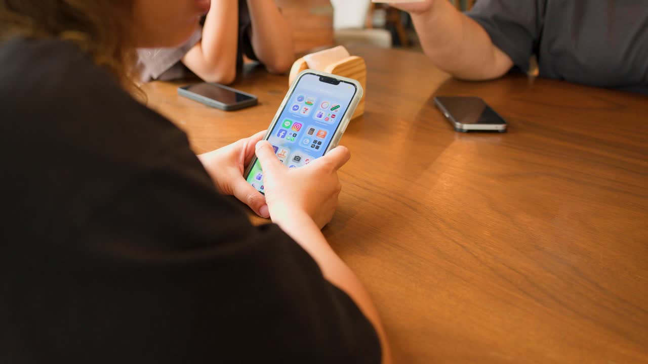 A person uses a smartphone at a wooden table in a brightly lit restaurant setting
