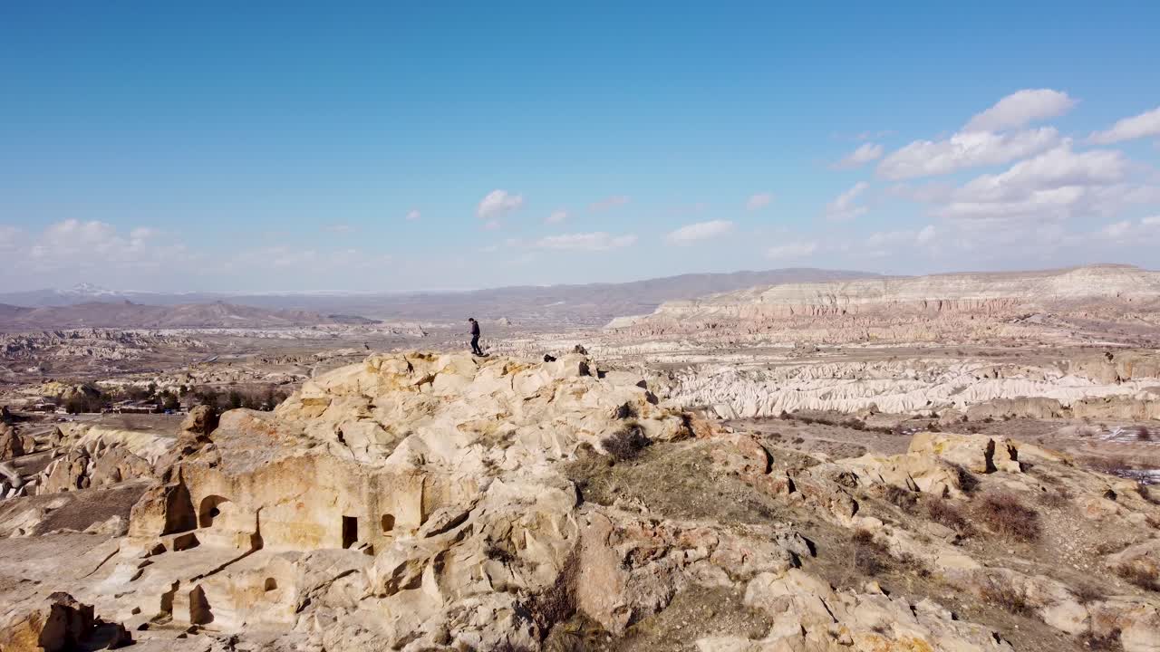 사막 계곡 탐험 어드벤처: 솔로 관광 하이커 산 동굴 거주지에서 지평선으로 걸어 가고, 고레메, 로즈 계곡을 향한 광활한 전망을 즐기고 있습니다.
