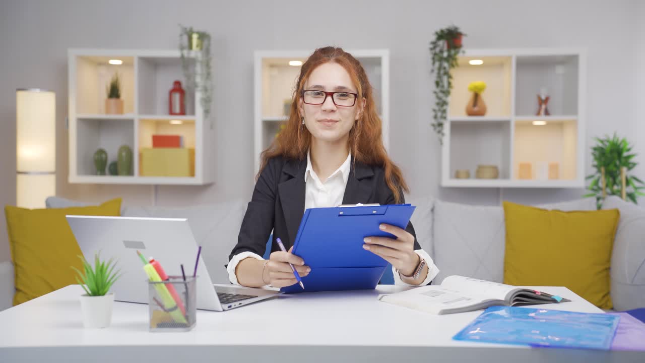 una mujer trabajadora de oficina en el hogar sonriendo a la cámara mirando el papeleo.