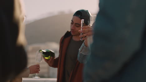 diverse group of friends celebrating rooftop party drinking alcohol young man pouring champagne enjoying reunion celebration at sunset