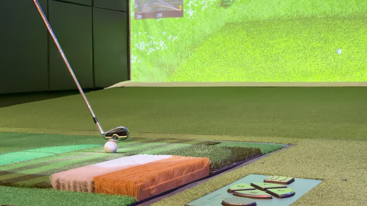Rallentatore ravvicinato di una mazza da golf che colpisce una pallina su un tappetino da simulatore da interno con proiezione