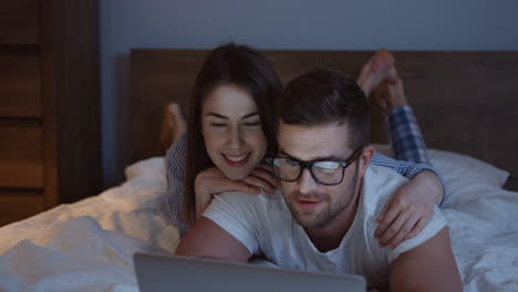 close-up view of the young couple lying on the bed in the evening and watching something funny on the laptop