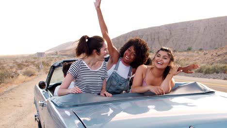 excited female friends in an open top car in the desert