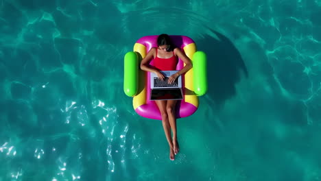 woman working on laptop while floating in a turquoise pool