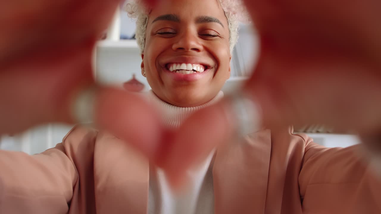 joven mujer afroamericana te mira sonríe dulcemente mostrando el corazón de las manos