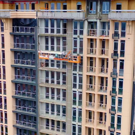 high-rise architecture under construction. workers on the outdoor lift doing the beautiful facade of multi-storey building.