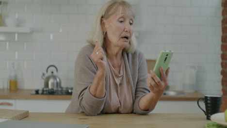senior woman having difficulty on video call in kitchen