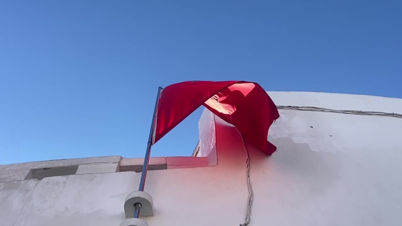 Flag of Morocco wind waving in slow motion as the sun's rays hit it in street