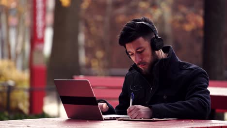 un hombre que estudia en su computadora portátil mientras escucha música en sus auriculares - plano medio