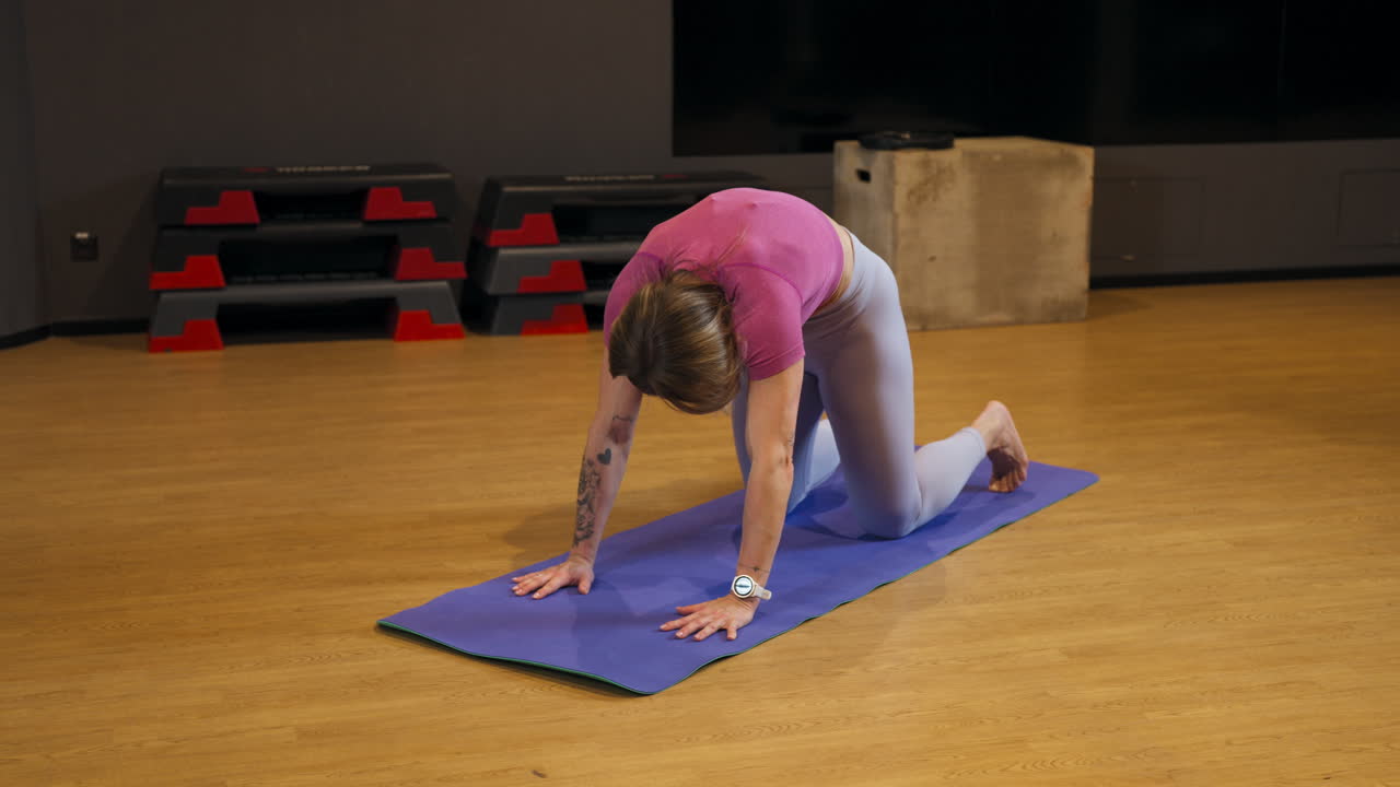 Middle-aged woman doing yoga breathing exercise on a mat in the gym