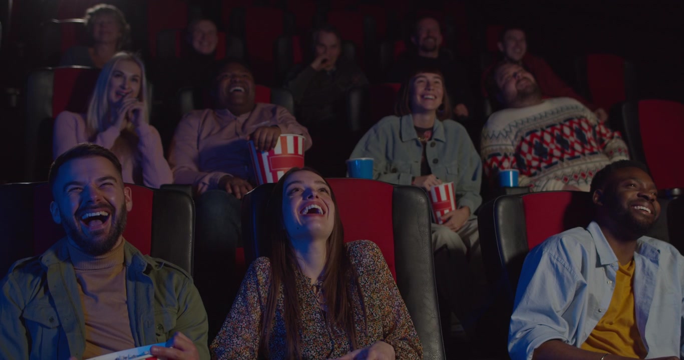 Grupo diversificado de amigos rindo enquanto assistem a um filme no cinema