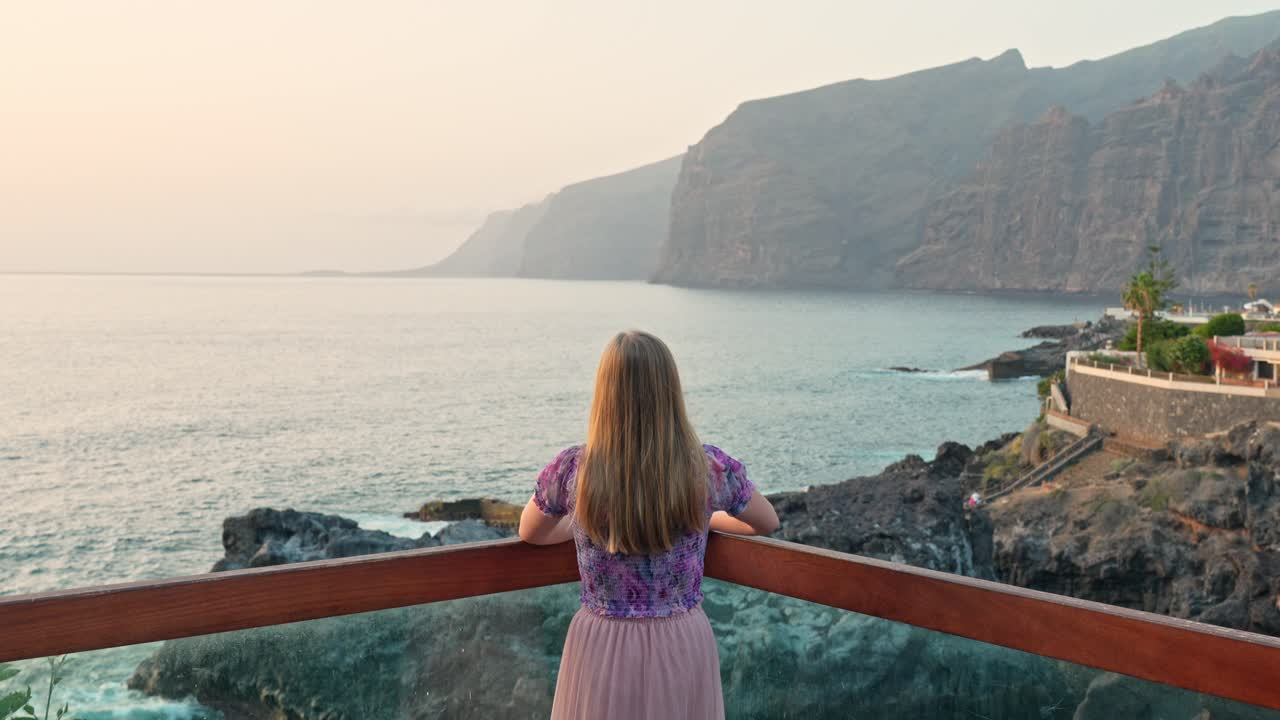 Young woman wear flowery pink dress admire Tenerife coast view from terrace