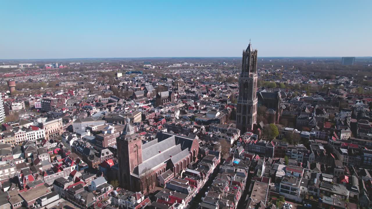 Approach aerial city center Utrecht, The Netherlands, on a bright sunny day with church and cathedral rising above the low build picturesque canal homes. Urban development and holland flat landscape