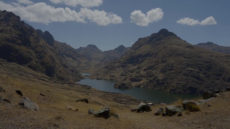 Ampia vista panoramica di un calmo lago glaciale blu circondato da maestose e aspre vette montuose nelle Ande peruviane. Paesaggio remoto ad alta quota, cielo azzurro soleggiato con nuvole, riprese panoramiche di viaggio