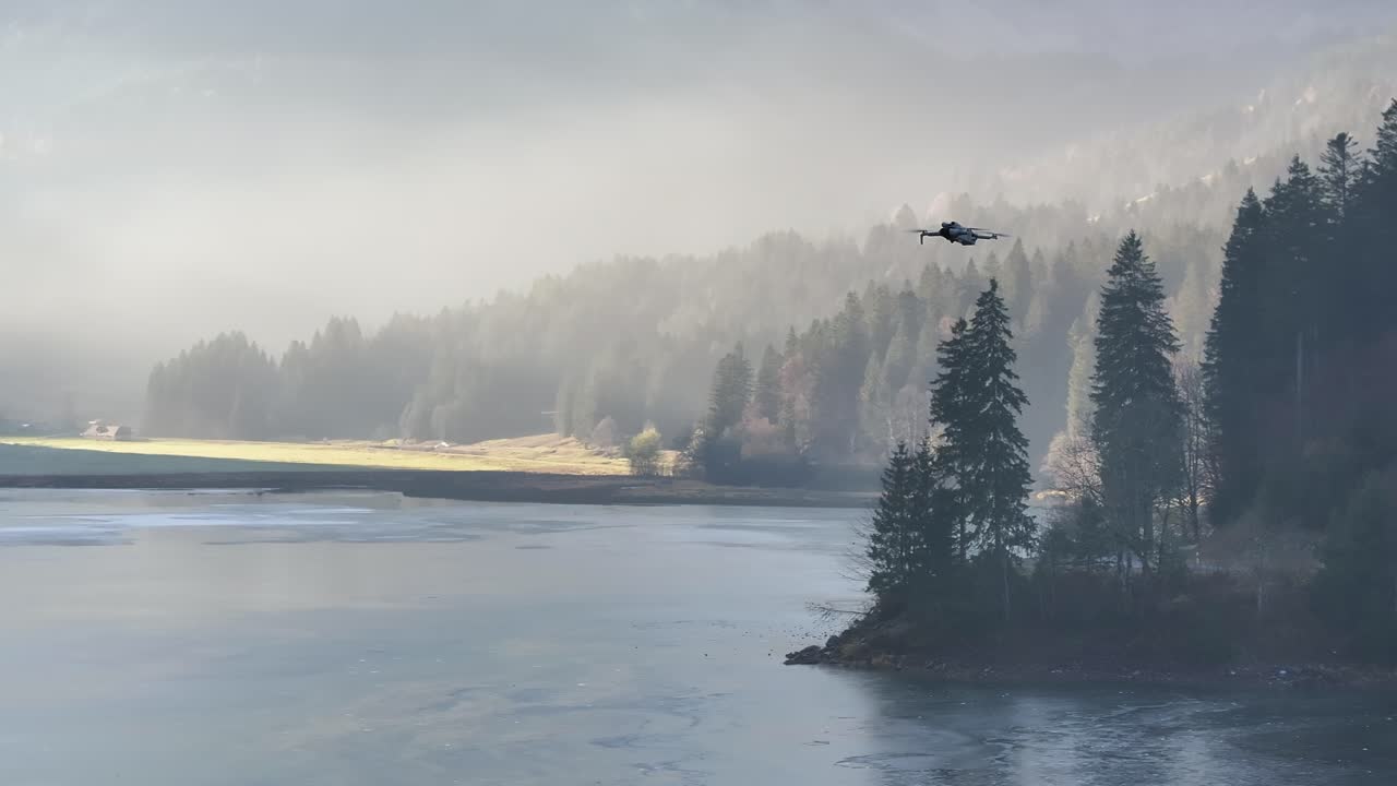 Drone flying over misty frozen lake with forested shore, Näfels, Glarus, Switzerland