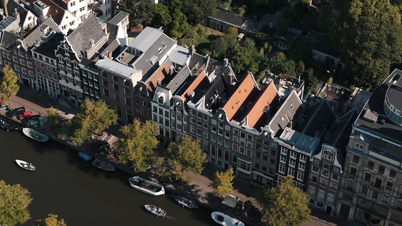Diagonal aerial tracking high angle across rooftops and canals in central Amsterdam district, urban backdrop