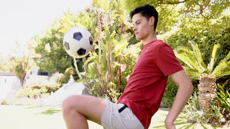 focused biracial man juggling football with thighs in sunny garden, copy space, slow motion