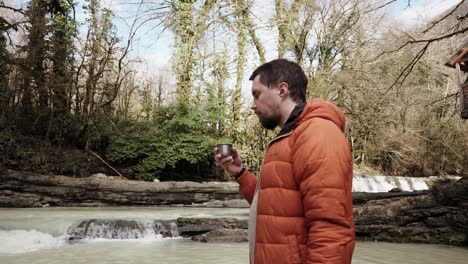 man drinking coffee by a waterfall in the forest