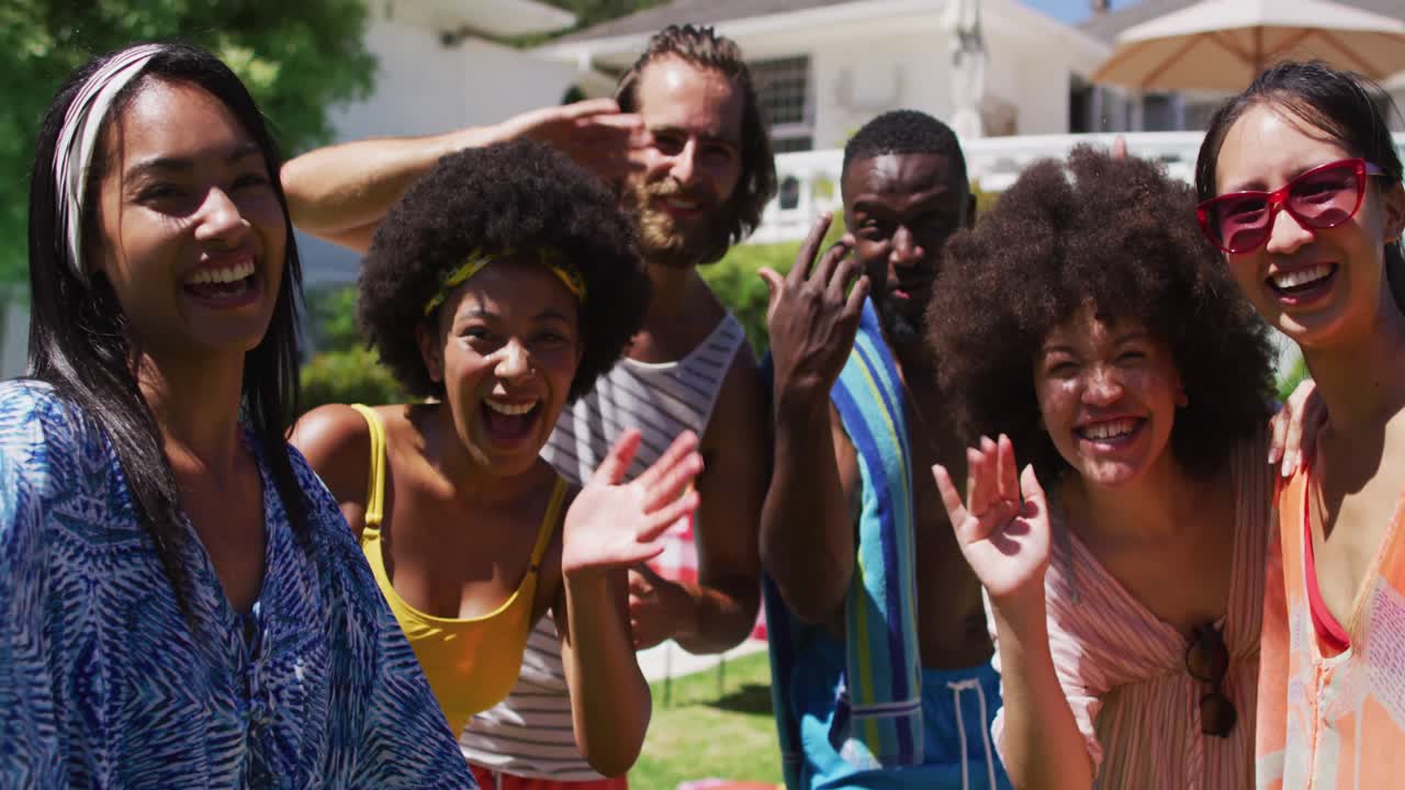 retrato de un grupo diverso de amigos sonriendo y saludando a la cámara en una fiesta en la piscina
