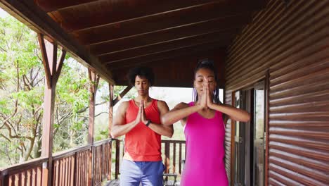 happy african american couple doing yoga and meditating in log cabin, slow motion