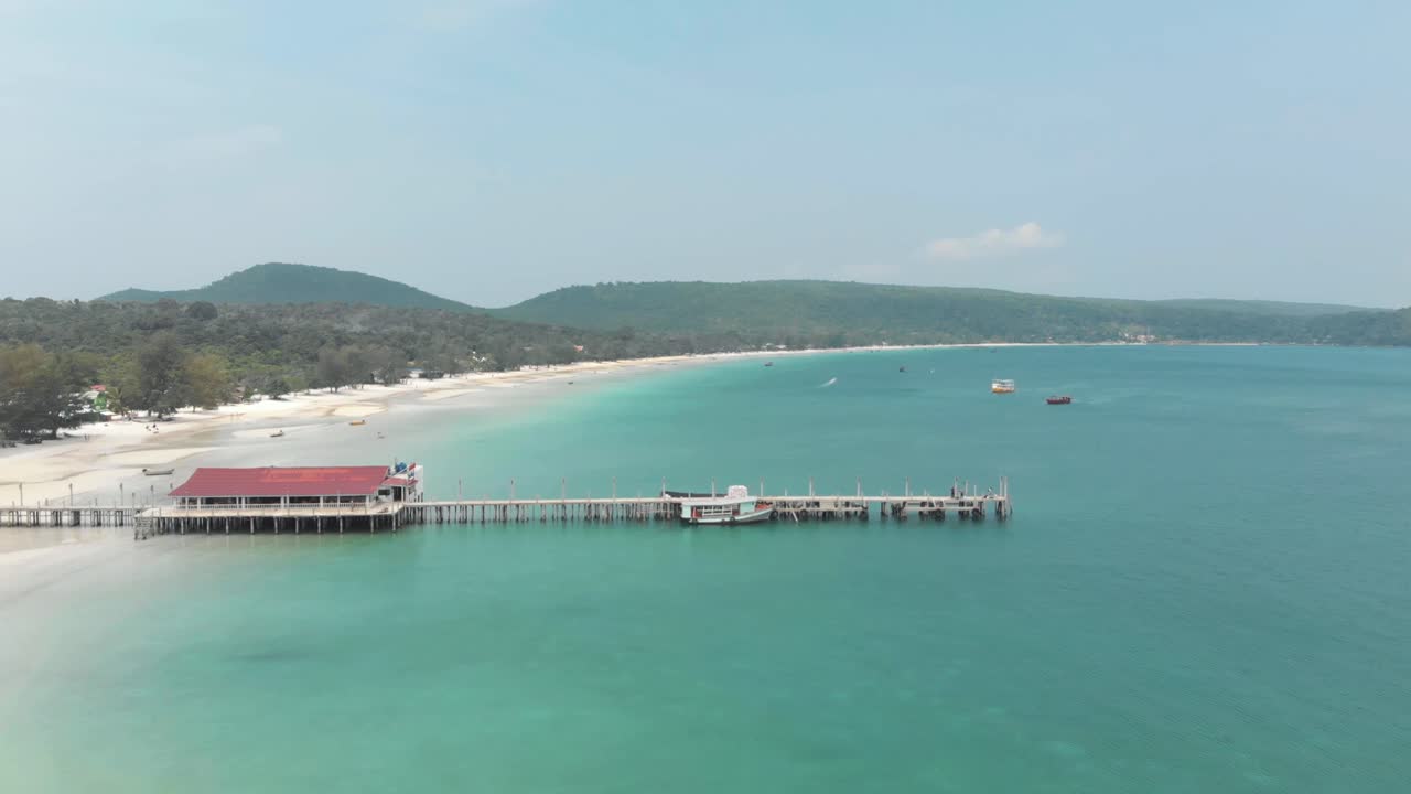 Cầu tàu gỗ cũ đứng trên mặt nước biển màu xanh ngọc lam tĩnh lặng và nông, chia cắt bờ biển bao quanh tại Vịnh Saracen ở Koh Rong Sanloem, Campuchia - Cảnh quay bay lượn từ trên không.