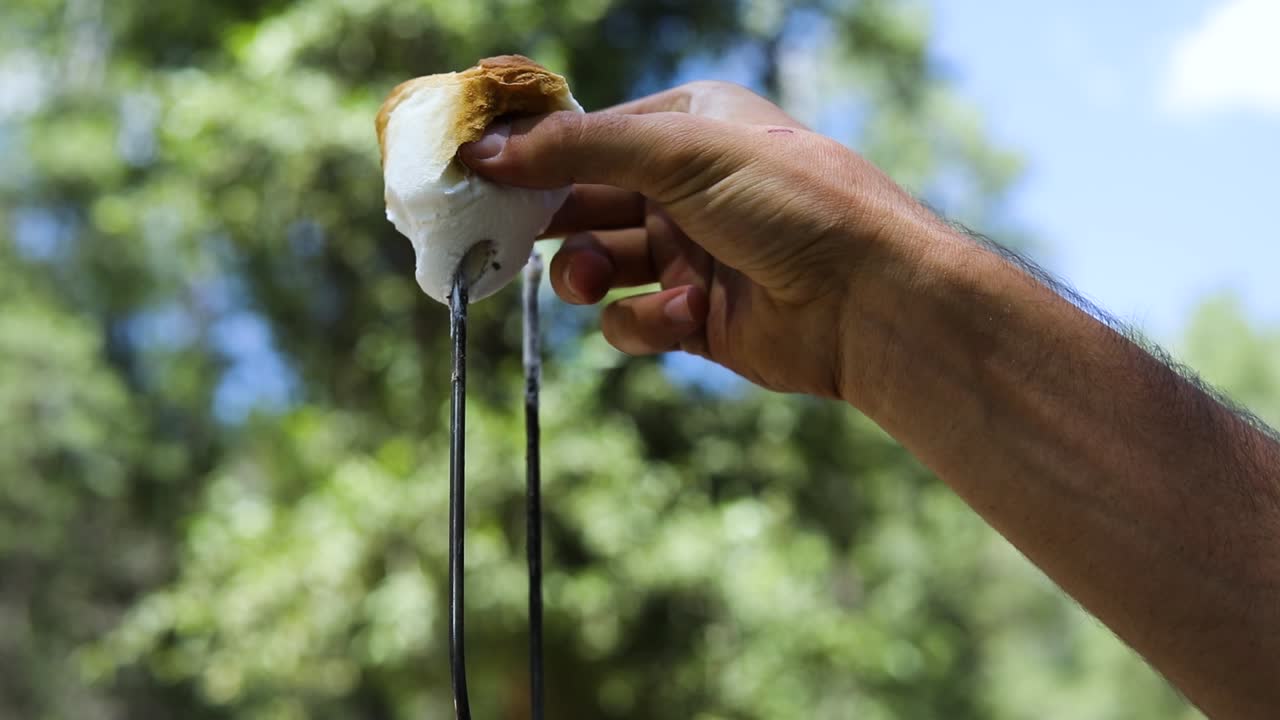 disparo en cámara lenta de alguien tirando de un malvavisco marrón dorado pegajoso de un pinchazo de metal para hacer s'mores