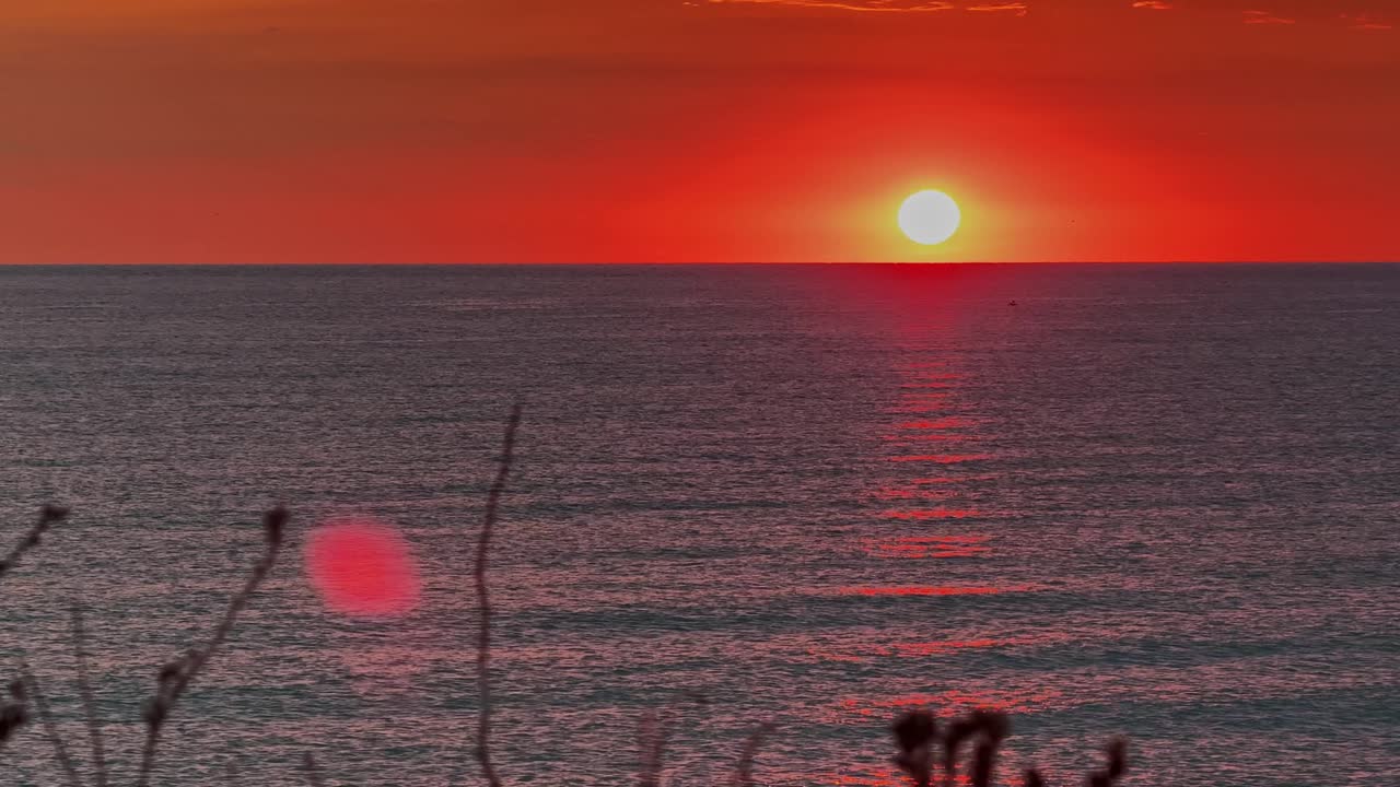 Sunset over calm ocean with vibrant orange sky, serene and peaceful vibe