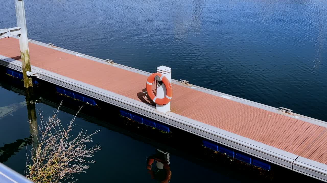 Empty wooden pier with orange life ring reflecting in calm waters at a harbor in Vigo Spain