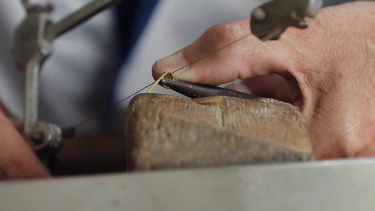 Goldsmith hands cutting a thin gold strip on a wooden bench pin with a jewellers saw