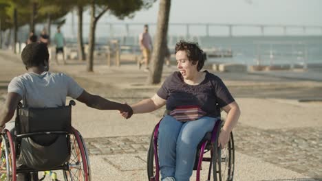 pareja de jóvenes positivas bailando usando sillas de ruedas tomados de la mano
