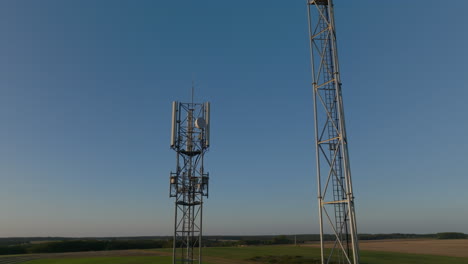 two cellular towers in the middle of farmland with sky background, aerial orbital closeup