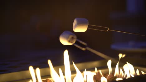 Two-delicious-white-marshmallows-roasting-over-gas-fire-pit-during-cozy-dusk