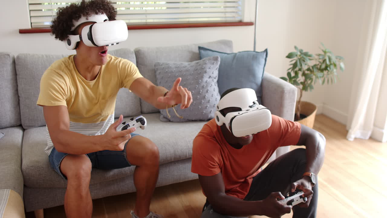 Playing video games with VR headsets, two multiracial male friends enjoying time together, at home