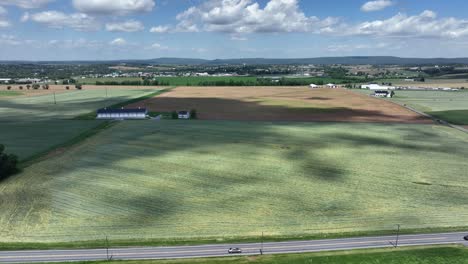 agricultural farm fields and driving cars on rural intersection road in america. aerial lateral wide shot. mountain range and small city in distance.