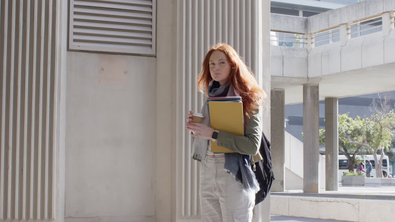 Žena držící šálek kávy, upíjející, poté přesouvá složku, pohlíží přes univerzitní chodník, s prostorem pro text.