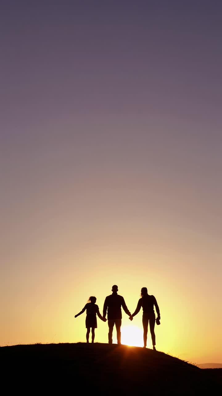 Famiglia in silhouette che si tiene per mano su una collina al tramonto, ripresa da un'angolazione bassa.