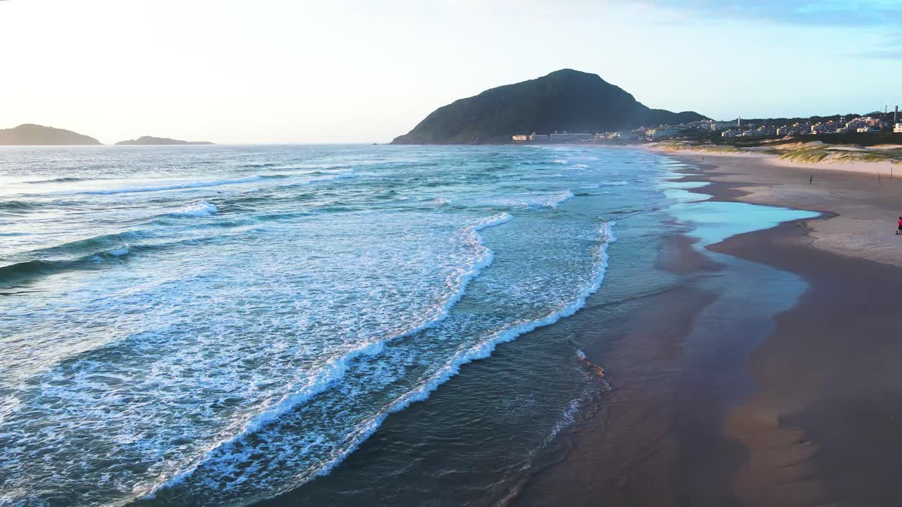Scena aerea di un drone che vola basso sulle onde del mare su una spiaggia paradisiaca a Florianopolis, la spiaggia di Santinho, con un uccello di passaggio.