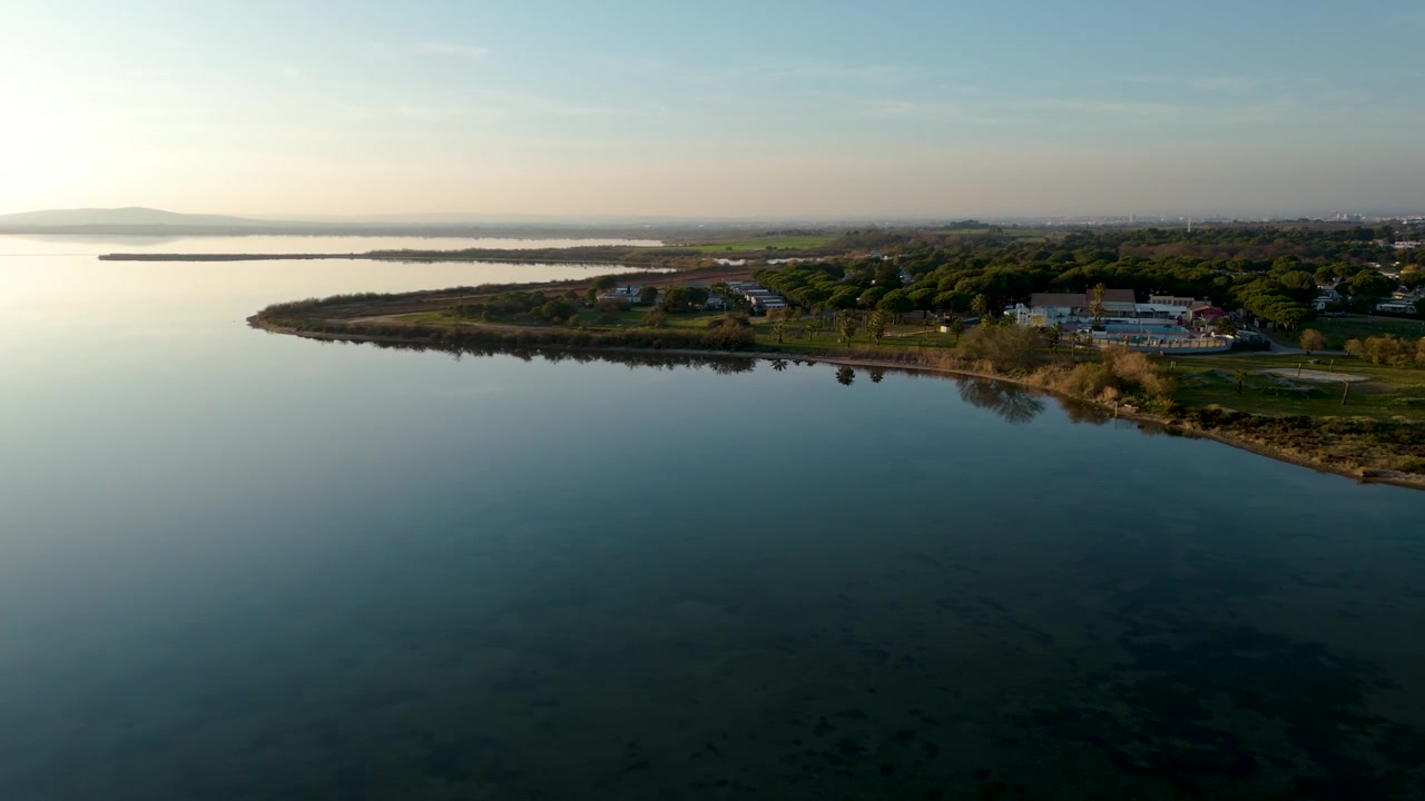 La costa dell'Etang de Thau si curva oltre acque calme, zone umide ed edifici in Francia, panoramica aerea di presentazione.