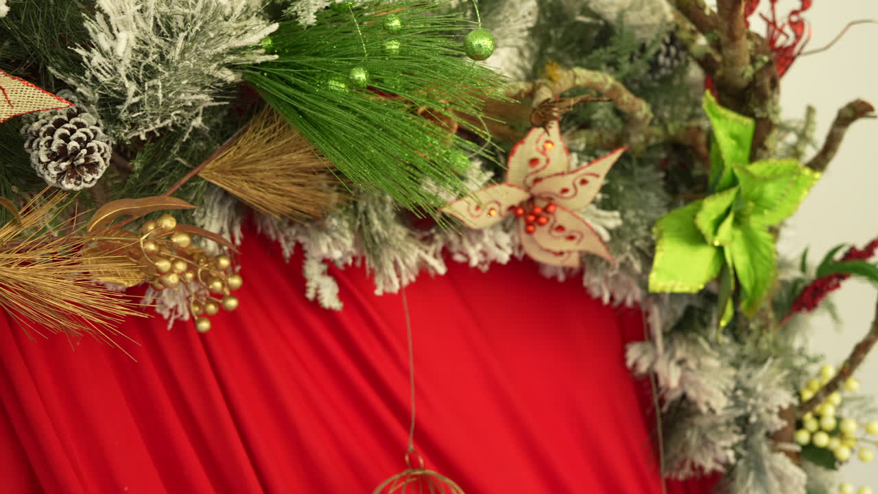 Captivating close-up of Christmas decorations with frosted pine cones, vibrant red fabric, and festive foliage. This shot captures intricate details under soft, warm lighting