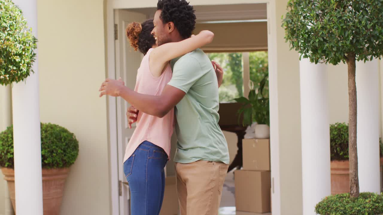 feliz pareja biracial sosteniendo las llaves de una nueva casa y abrazándose con alegría