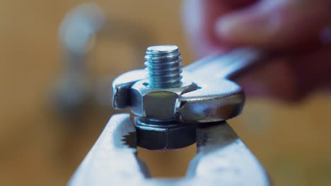 counterclockwise of a wrench turning a bolt off a screw held by pliers, close up