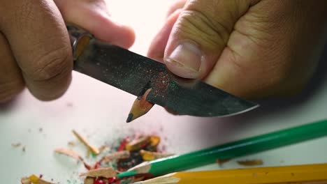 imágenes de manos afilando lentamente un lápiz y algunos lápices de colores con un cuchillo afilado