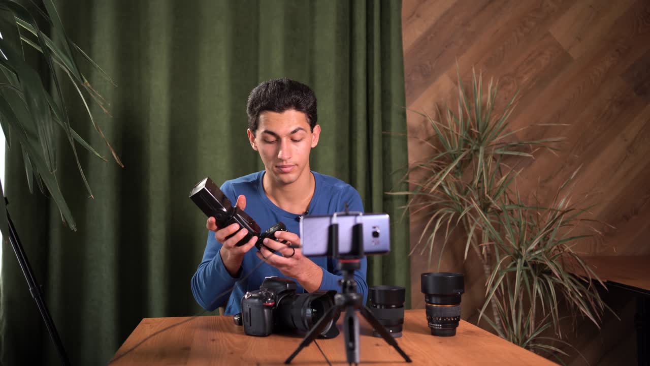 capacitación para fotógrafos principiantes, cursos en línea. un hombre musulmán graba una revisión de video de equipos fotográficos utilizando una aplicación en un teléfono inteligente. sincronizadores de radio su propósito