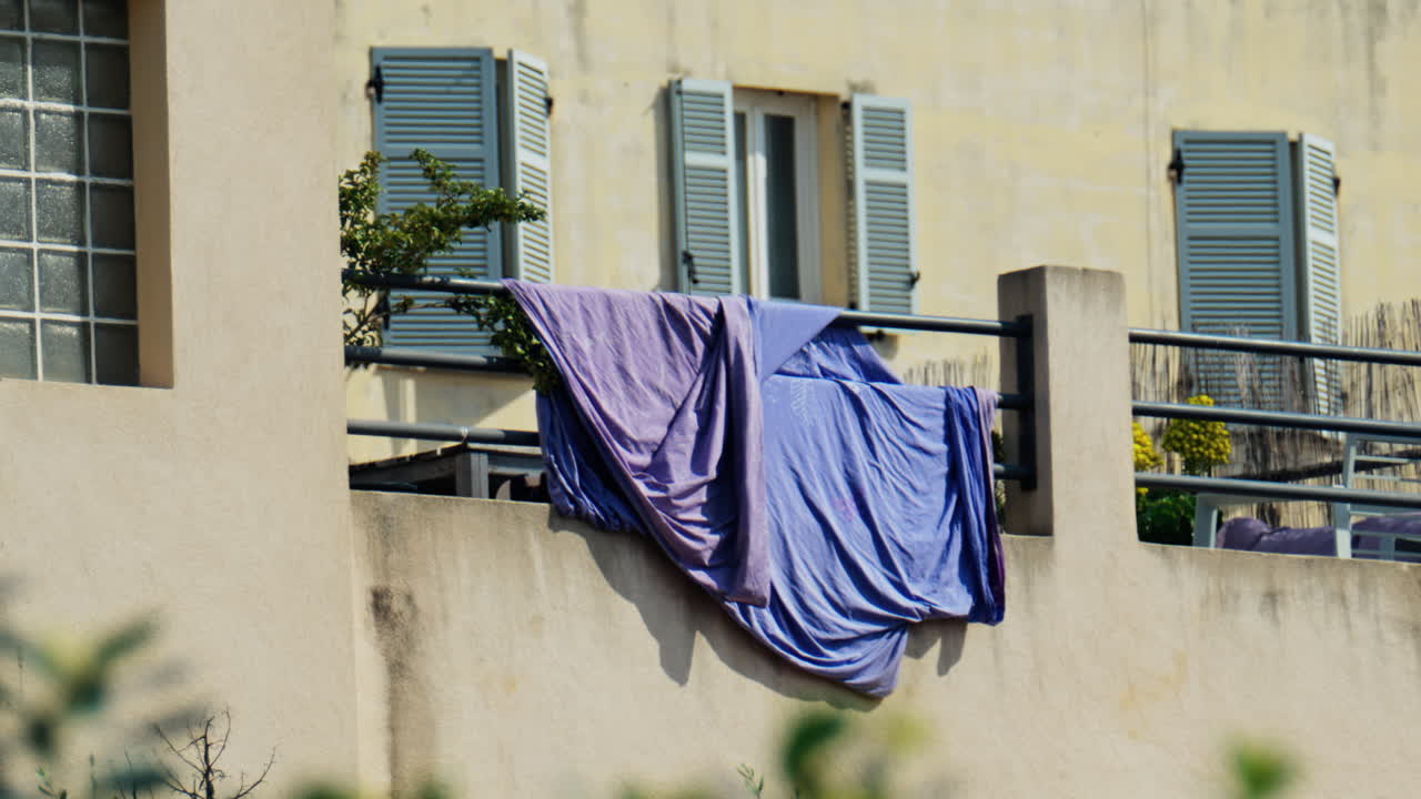 Purple bed sheets drying on a balcony on a sunny day