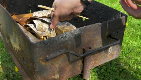 young man making the fire with safety matches and prepares rusty grill for baking and bbq, medium close up shot